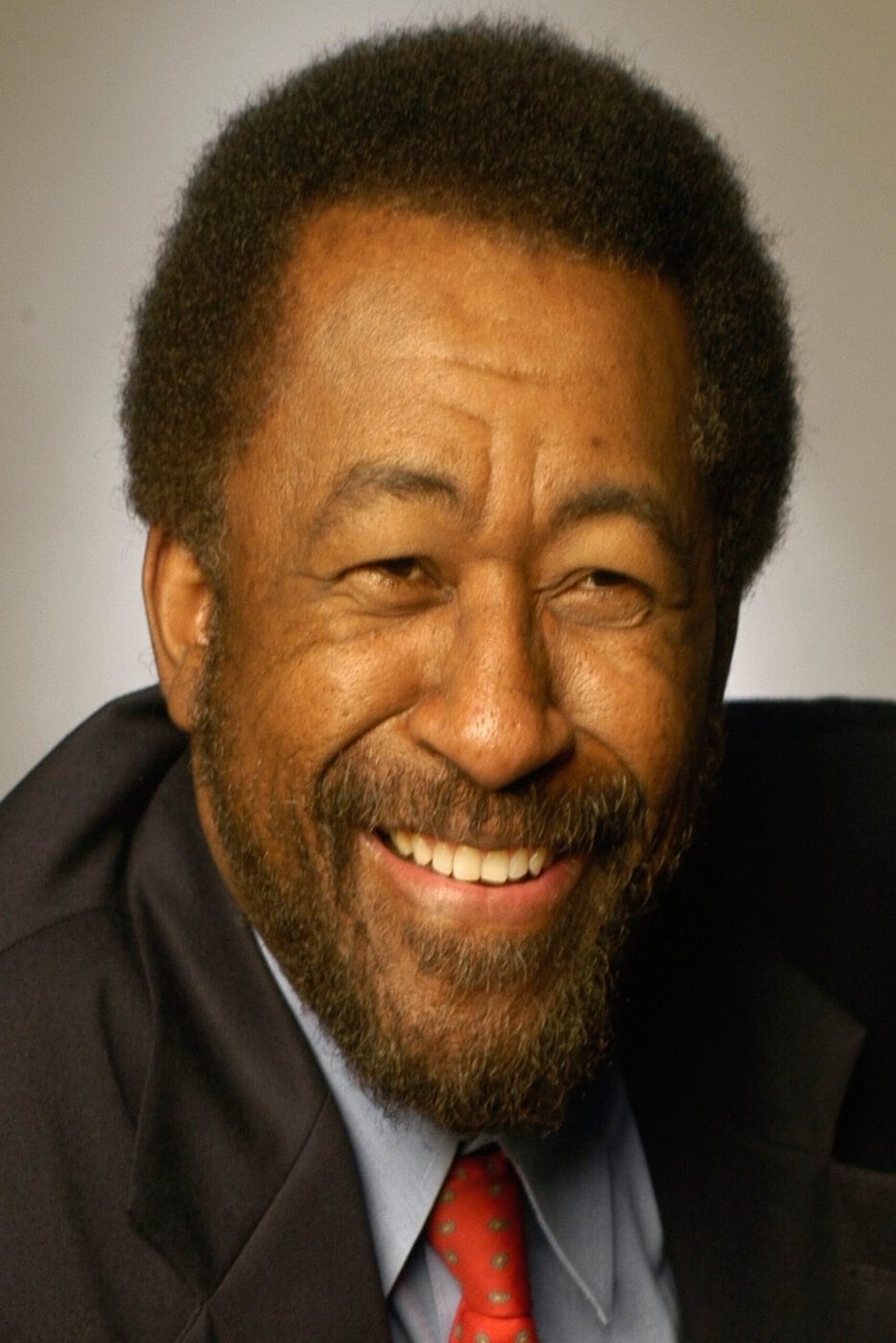 Portrait Of Radio Personality And Author Don Sainte-Johnn Smiling While Wearing A Dark Suit And Red Tie.
