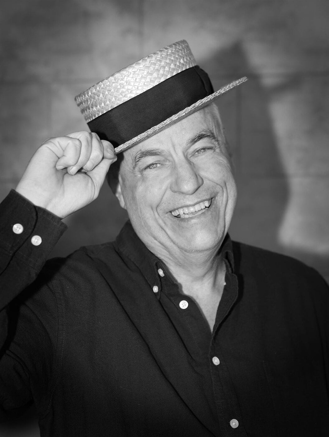 Robert Strom smiles while tipping a straw boater hat in a black-and-white portrait, reflecting the classic elegance and charm associated with the Fred Astaire era.